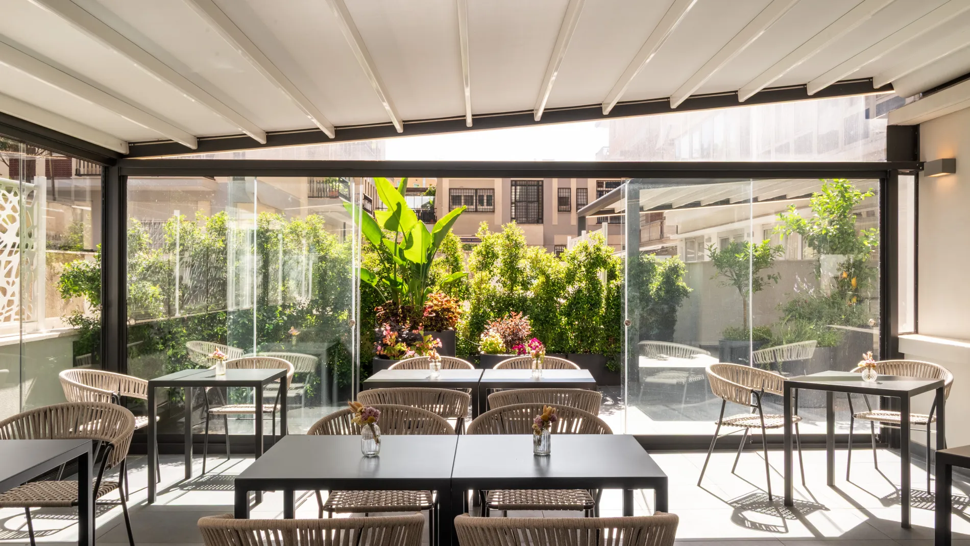 Covered terrace for breakfast and relaxation with tables, woven chairs and ornamental greenery - Aparthotel Colombo, BZAR hotels in Rome